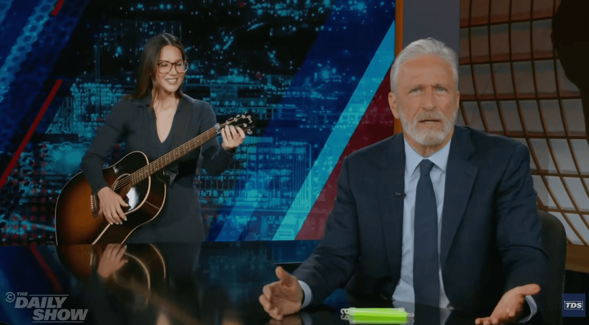 Jon Stewart’s ‘Daily Show’ Gets Surprise Visit From Olivia Munn In Sendup Of Stephen Colbert’s Goodbye Week: “No One Cares If You Leave”